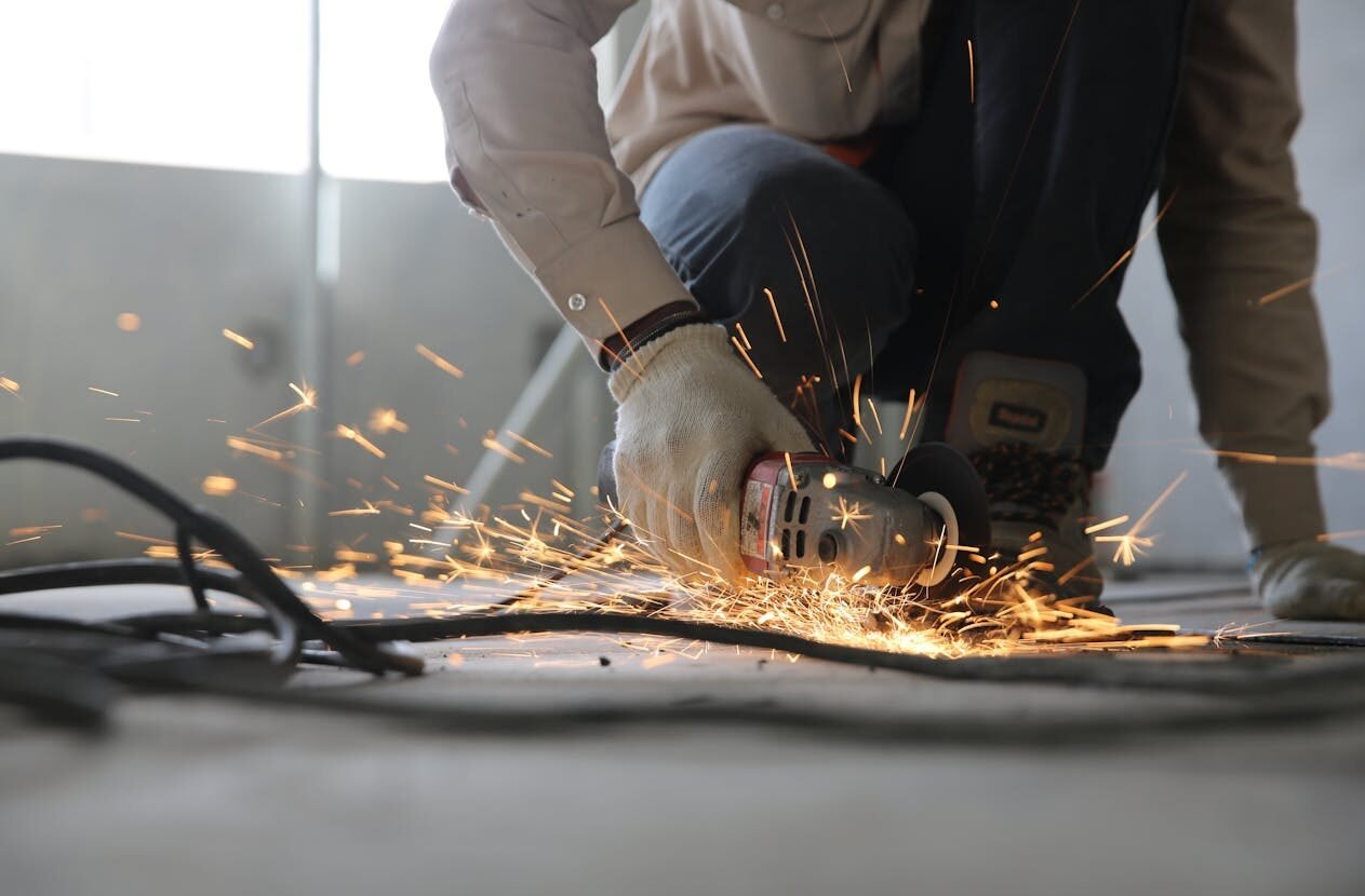 A skilled industrial worker uses a grinder creating a burst of sparks indoors.