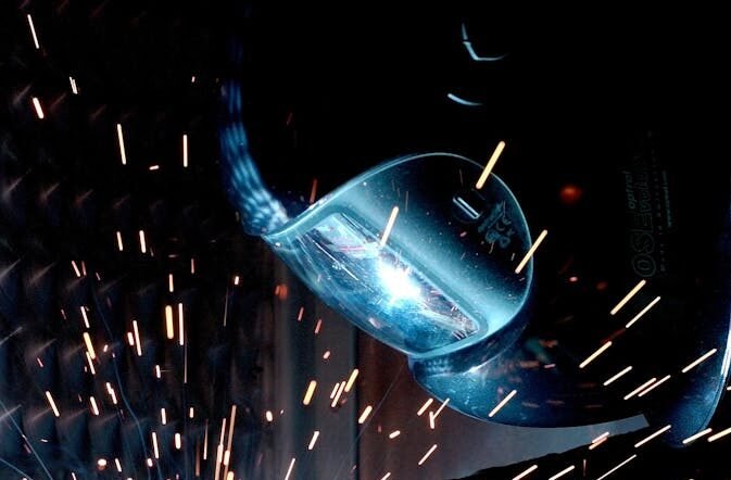 A focused welder works with metal in an industrial setting, creating vibrant sparks.